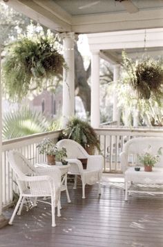 the porch is decorated with white wicker furniture and potted plants hanging from the ceiling