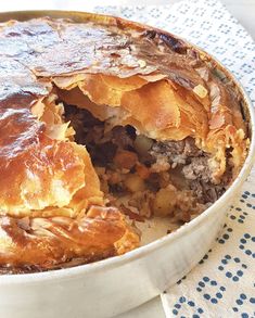 a pie with meat and potatoes in a metal pan on a blue and white table cloth