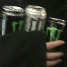 the person is holding three cans of monster energy drink in their hands, both with green letters on them