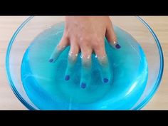 a person's hand on top of a bowl with blue water and purple nail polish