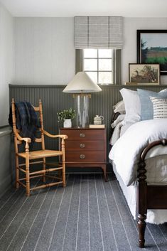 a bed room with a neatly made bed next to a dresser and lamp on top of it