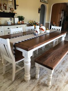 a kitchen table with two white chairs and a bench in front of the dining room table