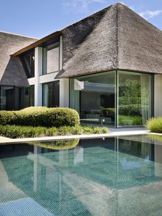 an outdoor swimming pool next to a large house with thatched roof and windows on the side