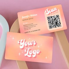 two pink business cards sitting next to each other on top of a wooden chair with a qr code