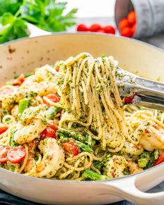 pasta with shrimp and pesto in a white skillet being stirred by a spatula