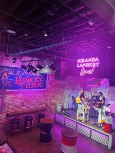 two men are playing instruments on stage in front of a brick wall with neon lights