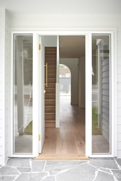 an open door leading to a house with white walls and wooden steps in front of it