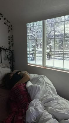 a person laying on a bed in front of a window with the snow outside it