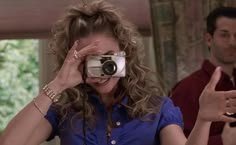 a woman holding a camera up to her face while standing in front of a man