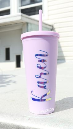 a purple cup with a straw in it sitting on top of a cement slab next to a building