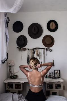 a woman sitting on top of a bed in a room with hats hanging above her head