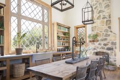 a dining room table and chairs in front of a stone wall with lots of windows