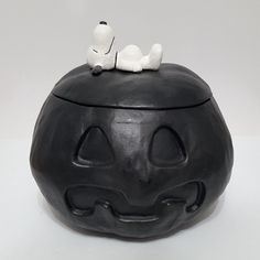 a black pumpkin shaped container with a white cat on top