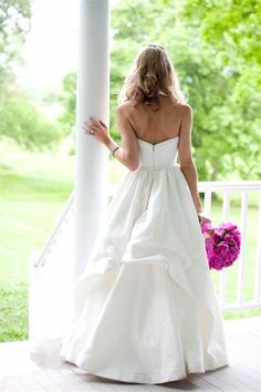 a woman in a white wedding dress is standing on the porch with her bouquet and looking back