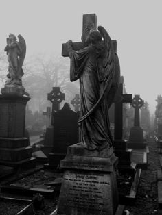 black and white photograph of an angel statue in a cemetery with tombstones on the ground