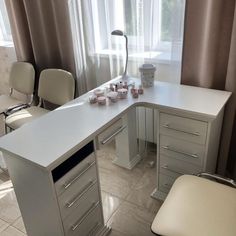 an office desk with several cups on it in front of two chairs and a window