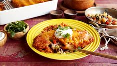 a yellow plate topped with mexican food next to other dishes and utensils on a table