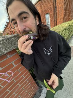 a young man eating a chocolate doughnut next to a brick wall