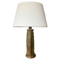 a table lamp with a white shade on the base and a gold leaf pattern design