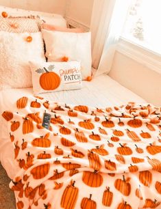 a bed with orange pumpkins on it next to a white pillow and blanket in front of a window