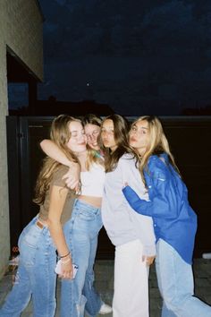 four girls are posing for the camera in front of a brick building at night, with their arms around each other