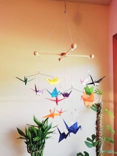 there are many origami birds hanging from the ceiling next to some potted plants