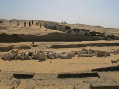 some people are standing in the sand near rocks and mud bricks on a sunny day