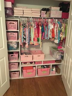 an organized closet with pink bins, baskets and clothes hanging on the wall next to it