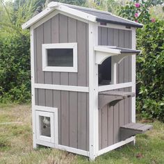 a gray and white dog house in the middle of some grass with bushes behind it