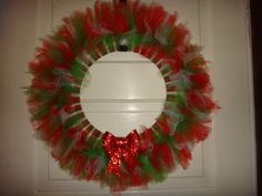 a red and green tulle wreath hanging on the front door with a bow around it