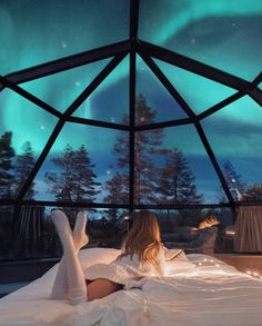 a woman laying on top of a bed under a sky filled with aurora bores