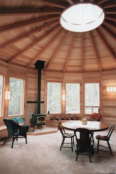 the inside of a wooden cabin with round table and chairs in front of an open fire place