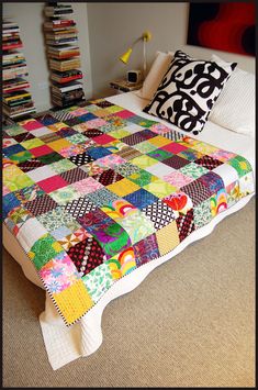 a bed with a colorful quilt on top of it next to a book shelf filled with books