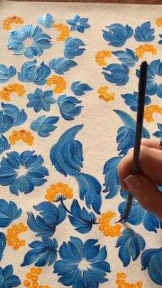 a hand holding a pen in front of a blue and yellow flowered design on fabric