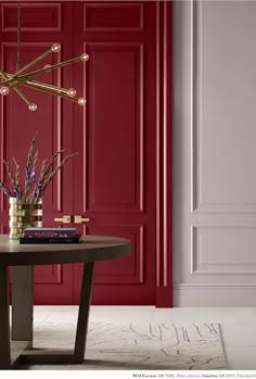 a living room with red walls and a round table in front of the wall is a gold chandelier