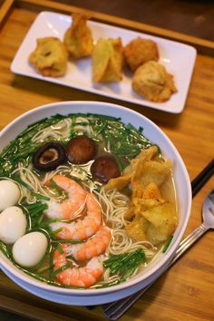 a bowl of ramen with shrimp, eggs and greens on the side next to silverware