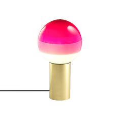 a pink and gold table lamp on a white surface with a black cord in front of it