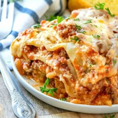 a white plate topped with lasagna covered in sauce and cheese next to bread