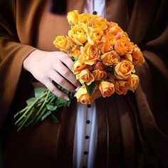 a woman holding a bouquet of yellow roses in her hands and wearing a brown coat