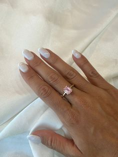 a woman's hand with white manicured nails and a pink diamond ring