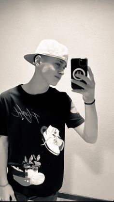 a young man taking a selfie with his cell phone while wearing a hat and t - shirt