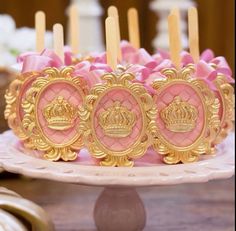 pink and gold decorated cake with candles in the shape of royal crowns on it's sides