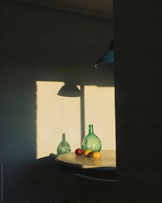 two green vases sitting on top of a table in front of a window with the sun shining through them