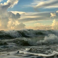 an ocean with waves crashing on the shore and clouds in the sky over it,