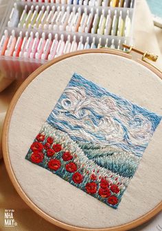 an embroidery project with red poppies in front of some scissors and other crafting supplies