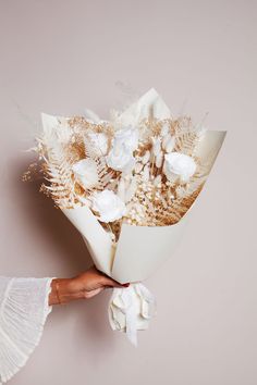 a woman holding a bouquet of flowers in her hand on a pink background with white petals