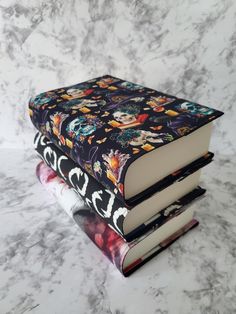 three books stacked on top of each other in front of a marble surface with skulls and flowers