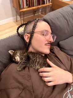 a man with glasses holding a cat in his lap while wearing a braid on top of his head