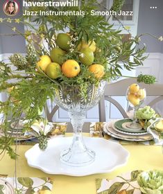 a vase filled with lots of fruit sitting on top of a white plate covered table