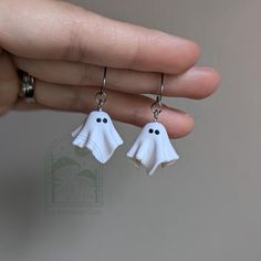 a pair of white ghost earrings with black eyes and hands holding it in front of the camera